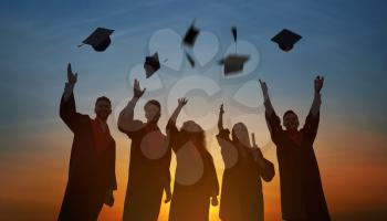 Silhouettes of students in bachelor robes throwing graduation hats outdoors at sunset�
