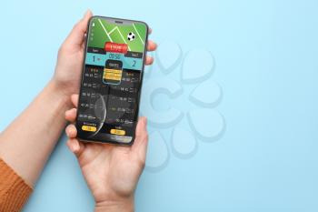 Female hands with open page of online betting site on screen of mobile phone against color background�