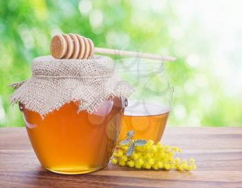 Honey in glass jars against nature bokeh background.