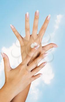 Two woman hands with moisturizer body cream against the sky