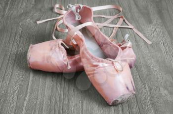 Old used pink ballet shoes on wooden background