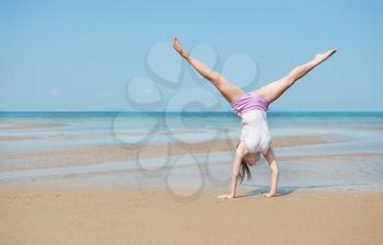 Beautiful energetic young woman doing handstand on the beach