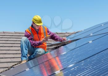 young worker checking solar panels on house roof