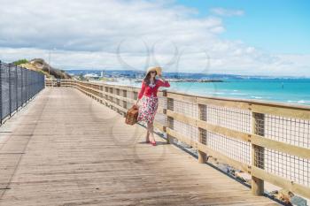 Adelaide seafront view and beautiful lady in red walking along wooden deck.Focus on the woman
