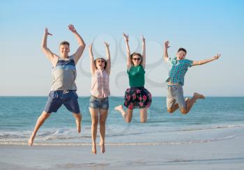Group of young happy friends have fun  on the beach together jumping up at sunset