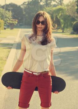 Beautiful young girl with skateboard  in the evening light with vintage instagram style toning