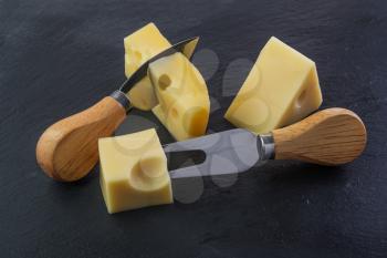 Three pieces of cheese on a black stone slate plate with knife and fork