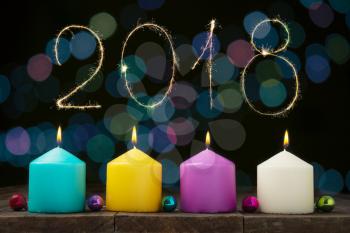 Multicolored burning candles with bokeh and digits 2018 on black background.Concept of New Year and Xmas