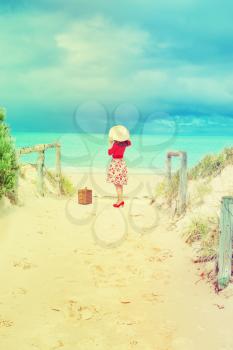 Beautiful lady in red traveler with wicker suitcase on the beach in retro style 