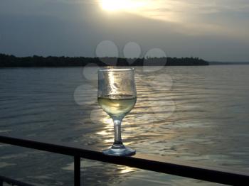Royalty Free Photo of a Glass of Wine on a Railing at Sunset