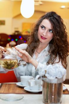 Pretty young woman pours tea into a cup