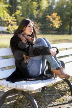 Attractive young woman sitting on a bench in autumn park