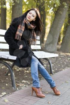 Cute young woman sitting on a bench in autumn park