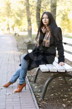 Lovely young woman sitting on a bench in autumn park