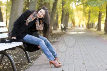 Smiling young brunette sitting on a bench in autumn park