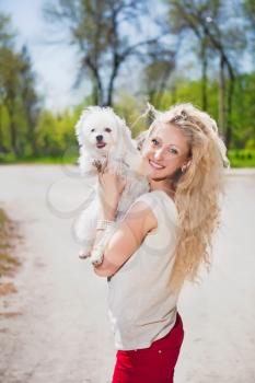 Pretty blond woman posing with white dog in the park