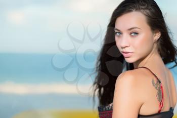 Portrait of beautiful young brunette with tattoo posing on the beach