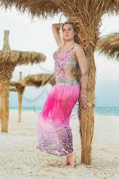Sexy blond woman posing in pink dress near the palm