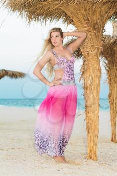 Elegant blond woman posing in pink dress near the palm