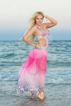Sexy young woman in pink dress posing on the beach