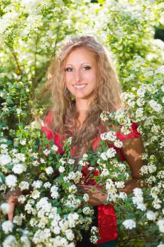 Curly young blond woman posing near the flowering bush