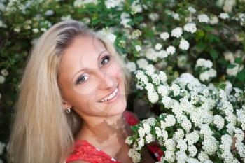 Portrait of pretty smiling blond woman posing near the flowering bush