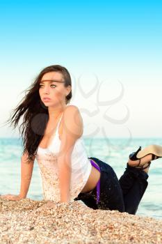 Charming young woman in wet shirt and jeans posing on the beach
