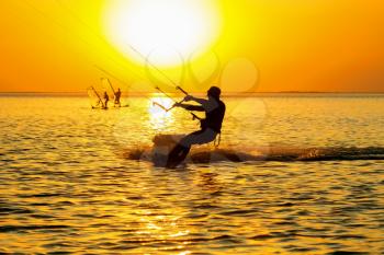 Silhouettes of a windsurfers sailing in the gulf at sunset