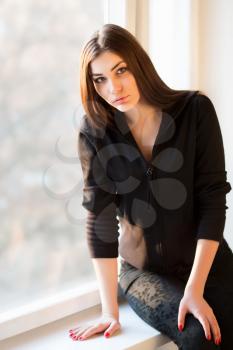 Portrait of attractive young brunette sitting on the windowsill
