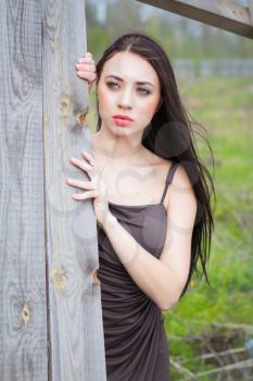 Pensive young brunette posing near the wooden fence