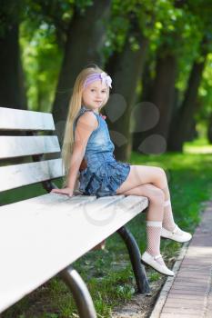 Blond little girl sitting on the white bench