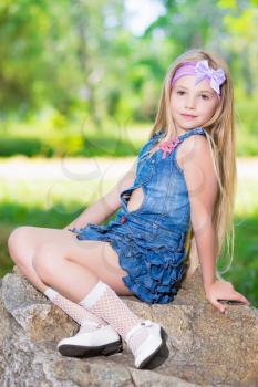 Little girl in blue jeans dress sitting on the stone