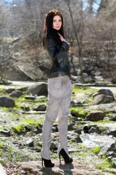 Young brunette in black jacket and light pants standing on the rock