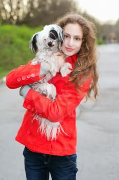 Young curly brunette in red jacket hugging little dog