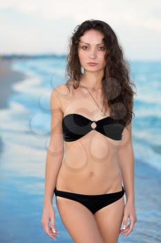 Pretty brunette in black swimsuit posing on the beach