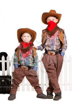 Two boys in cowboy costumes posing near the fence. Isolated on white