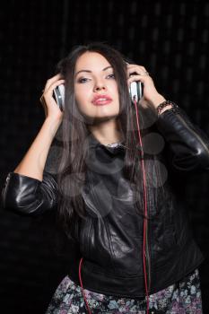 Pretty young black-haired woman posing with headphones. Isolated on black