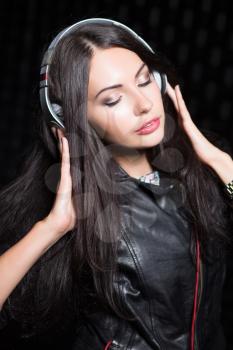Portrait of pretty brunette posing with headphones and closed eyes. Isolated on black
