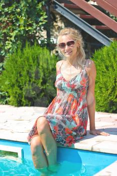 Beautiful girl sits on pool edge on summer dress