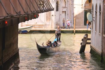 VENICE, ITALY - MAY 06, 2014: Gondolier sails with tourists sitting in a gondola down the narrow channel in Venice, Italy