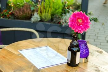 Flower in a bottle, candle and menus on the table in an outdoor cafe