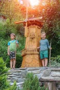 Two boys next to small mill in summer city park in sunlight