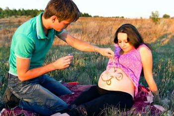 guy draws a face on a stomach of pregnant woman