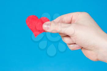 Red paper heart in hand, over a blue background