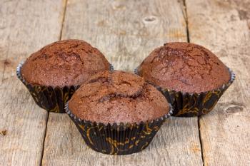 Three chocolate muffins on a wooden plank