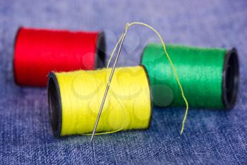Colorful bobbins with needle on jeans material