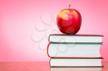 Red apple on the books with a pink background