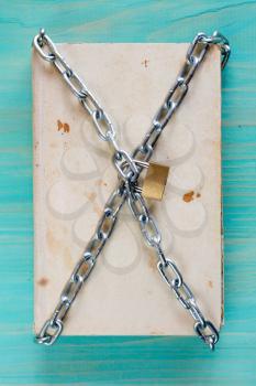 Old book with chain and padlock on blue table