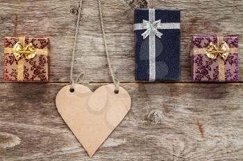 Blank heart shaped tag and three gift boxes on wooden background