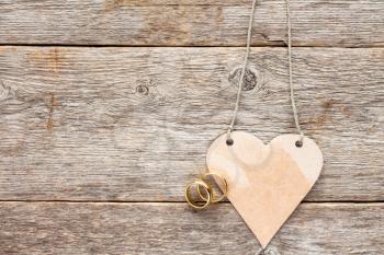 Gold wedding rings and paper heart nanging on wooden background
